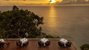 A terrace with tables and chairs overlooking the sea at sunset.