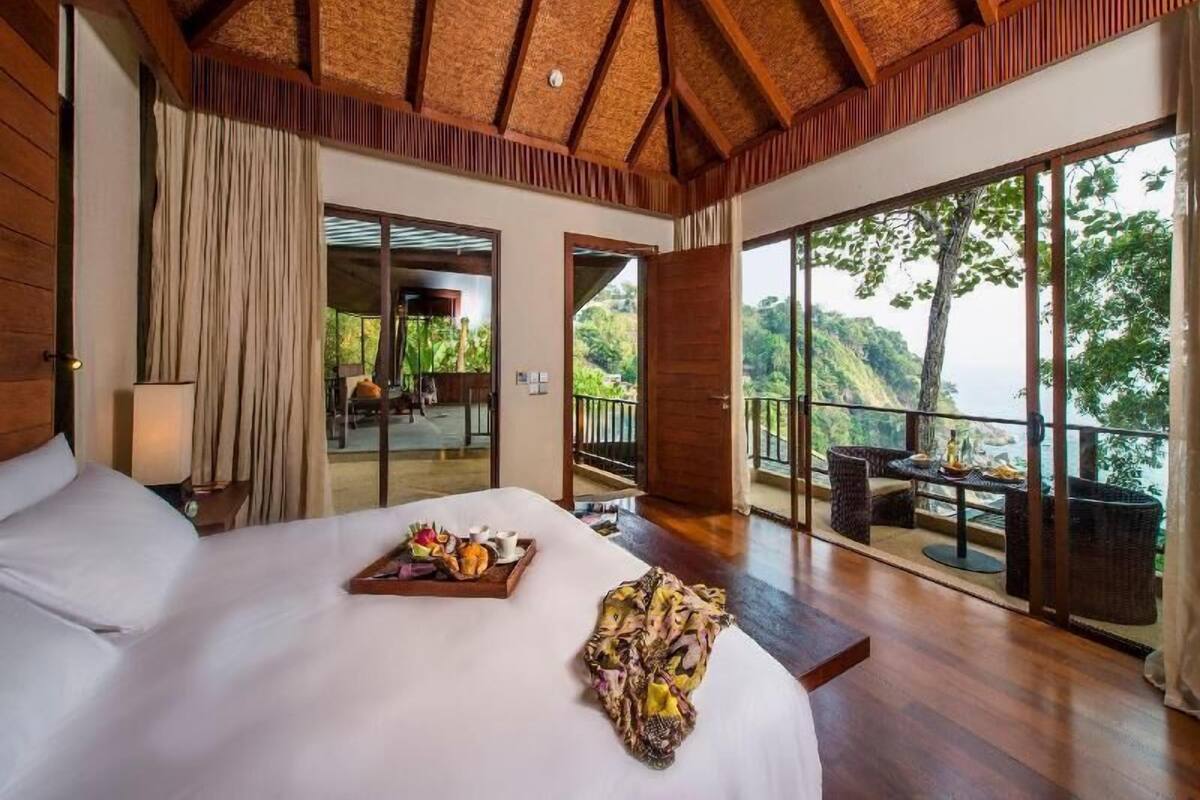 Um quarto espaçoso com uma cama grande, uma mesa de jantar com cadeiras e uma varanda com vista panorâmica.