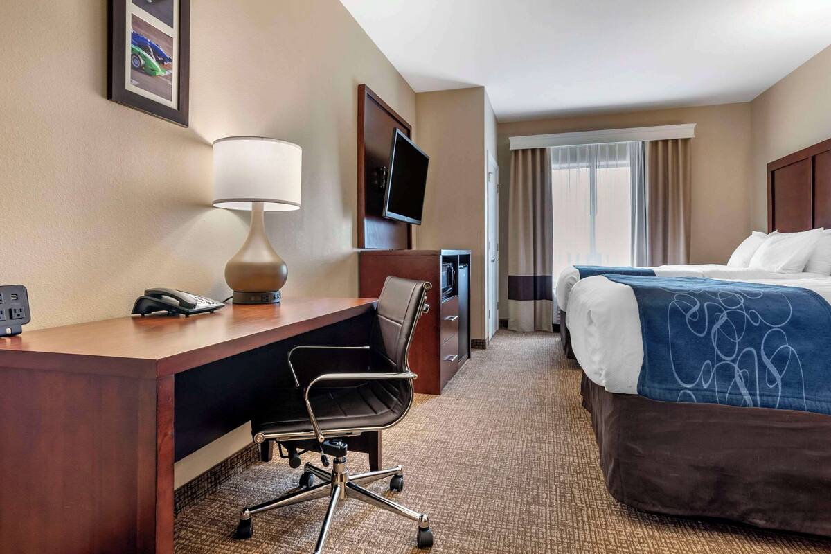 A hotel room with a desk, chair, bed, TV, and a window with curtains.