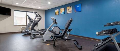 Ein Fitnessraum mit Cardiogeräten, einem an der Wand montierten Fernseher und Kunstwerken.