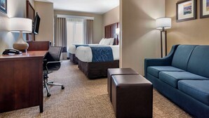 A hotel room with a desk, two beds, a sofa, and a TV.
