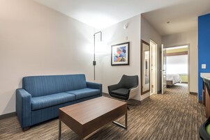 Una habitación de hotel con un sofá azul, una mesa de centro de madera, un sillón negro y una obra de arte abstracto enmarcada en la pared.