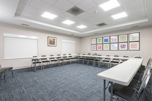 Un salón de conferencias con una larga mesa, sillas, una pizarra y cuadros en la pared.