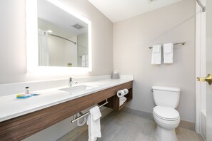 A modern bathroom with a white sink, wooden vanity, a large mirror, a toilet, and a towel rack.