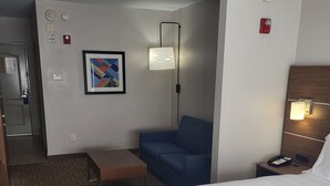 Une chambre d’hôtel avec un lit, un canapé bleu, une petite table, une lampe fixée au mur et un tableau encadré.