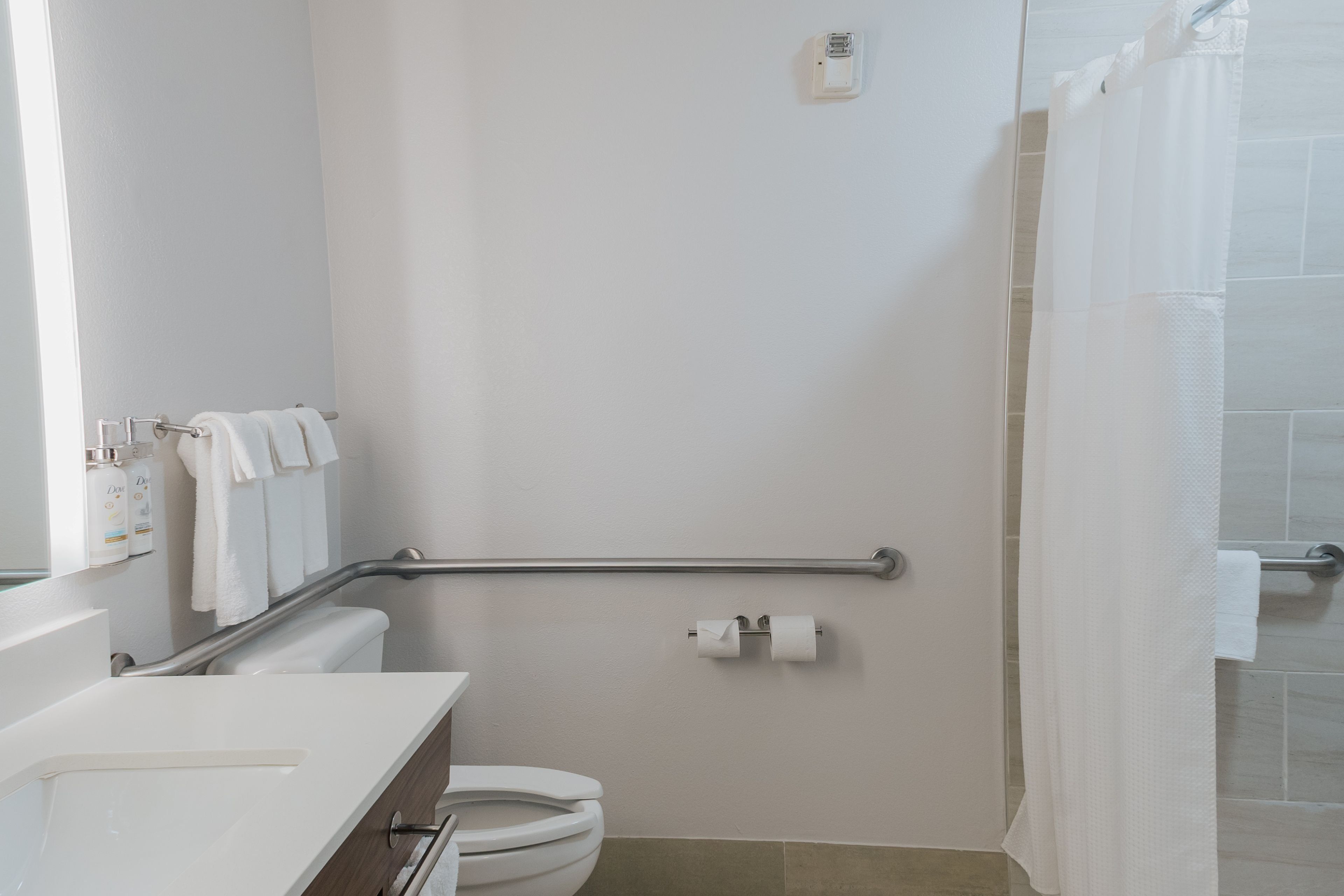 A bathroom with a toilet, a handrail, a towel rack, and a shower curtain.