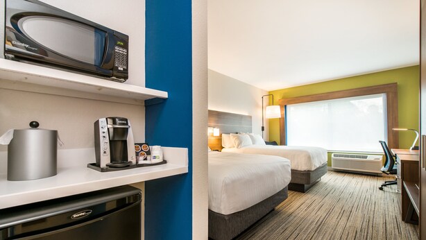 Une chambre d’hôtel équipée d’un four à micro-ondes, d’une machine à café et d’un petit réfrigérateur. La chambre comprend deux lits, une grande fenêtre et un appareil de climatisation.