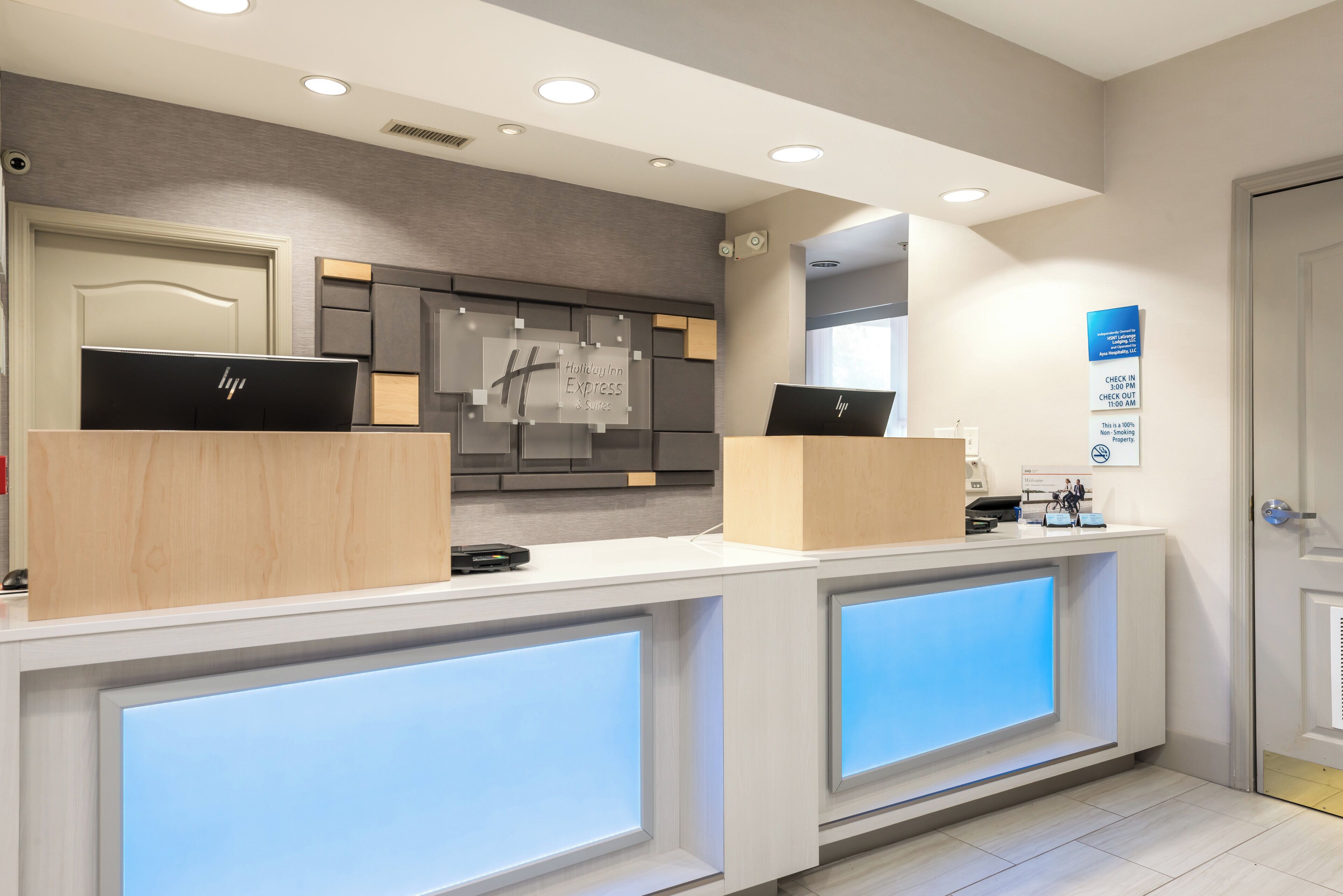 A hotel reception desk with two HP laptops, a digital check-in/out board, and a modern interior design.