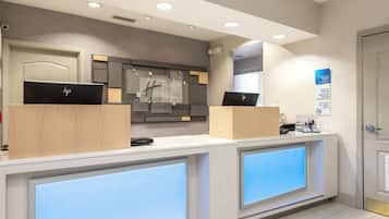 A hotel reception desk with two HP laptops, a digital check-in/out board, and a modern interior design.