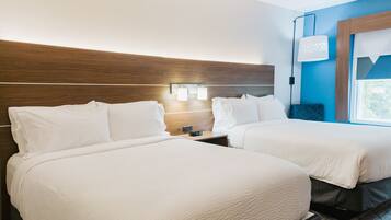 A hotel room with two beds, a nightstand, a lamp, and a window with a view.