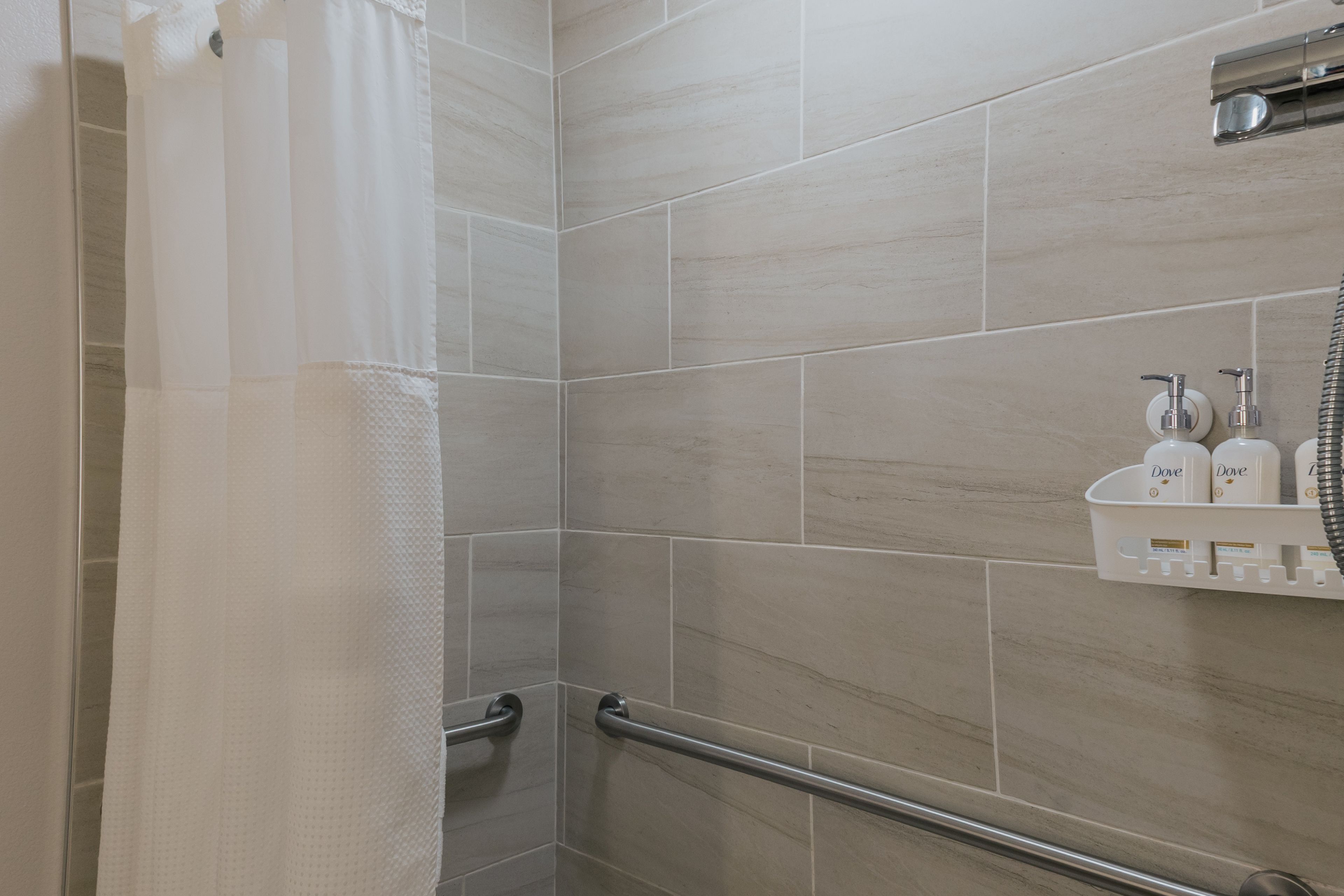 A bathroom with a shower area, a handrail, and a shelf with toiletries.