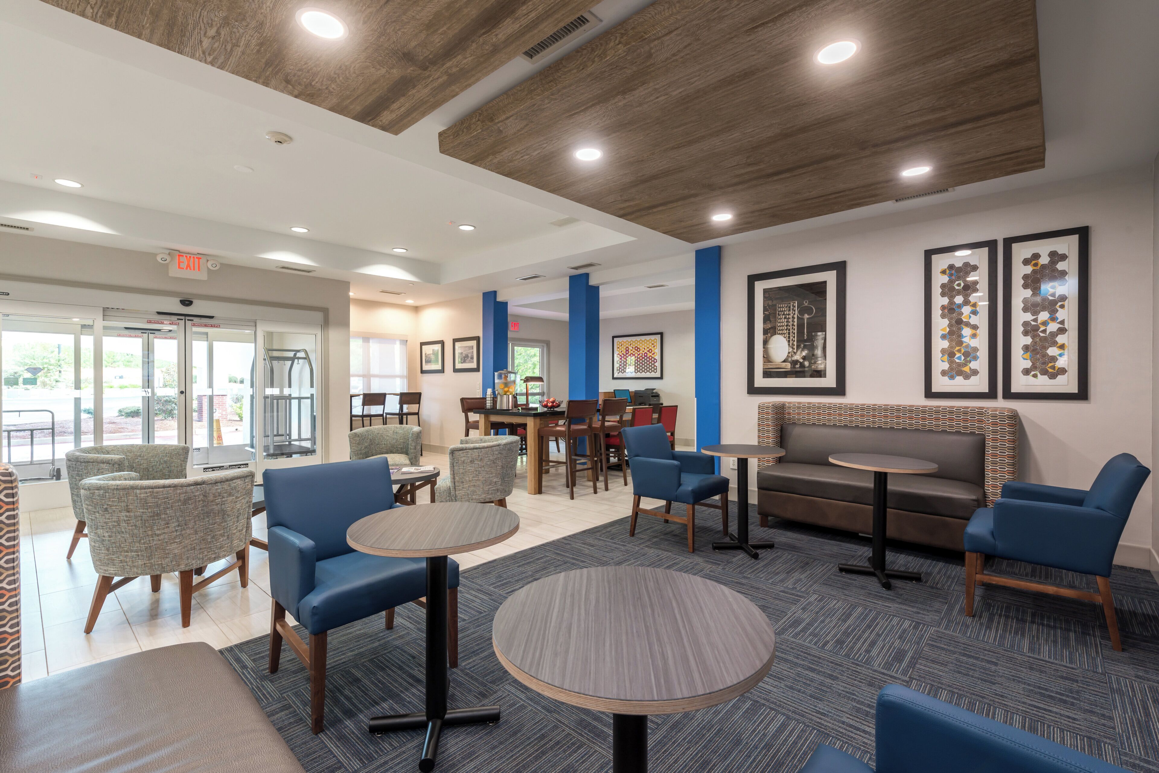 A modern indoor seating area with round tables and blue chairs, a sofa, and a patterned wall.