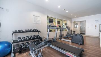 Un gimnasio con cintas de correr, elípticas y un estante con mancuernas.