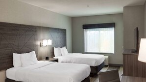 Une chambre d’hôtel avec deux lits, un bureau, une chaise, une télévision et une fenêtre avec des stores.