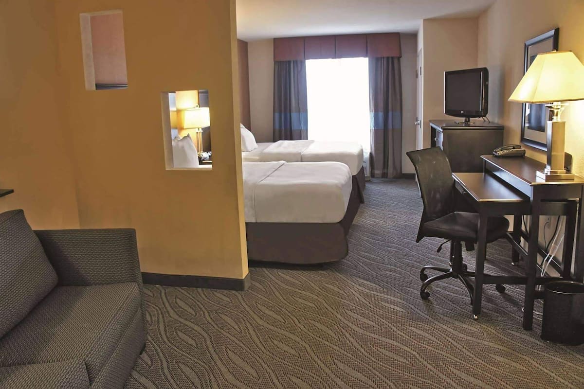Een hotelkamer met een bed, een bureau met een computer, een stoel, een televisie en een lamp.