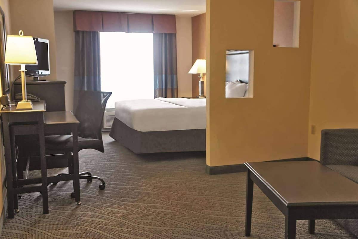 Een hotelkamer met een bed, bureau, stoel, lampen en een klein tafeltje.