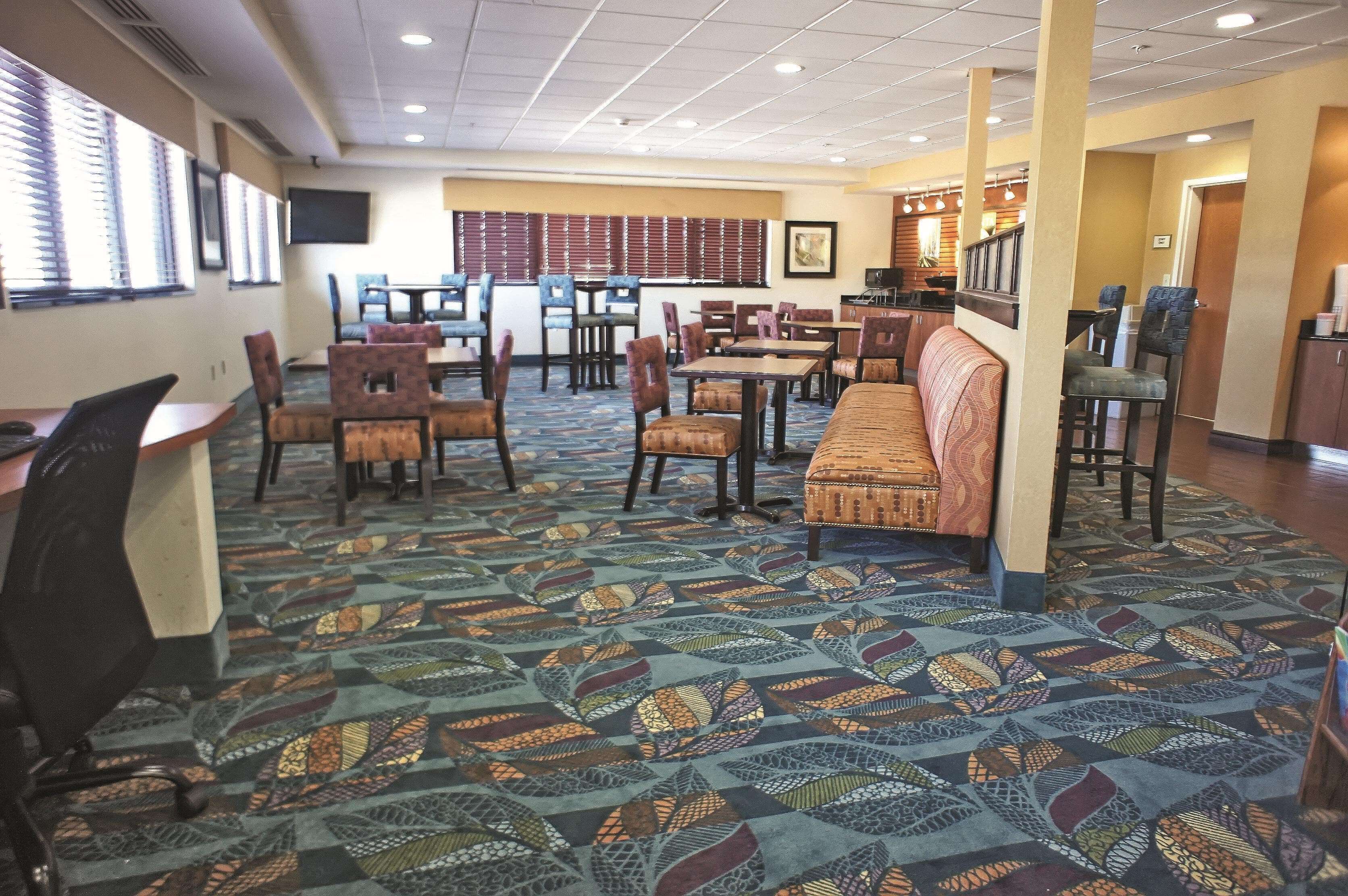 A hotel lobby with multiple seating areas, including tables and chairs, a patterned carpet, and a bar area.