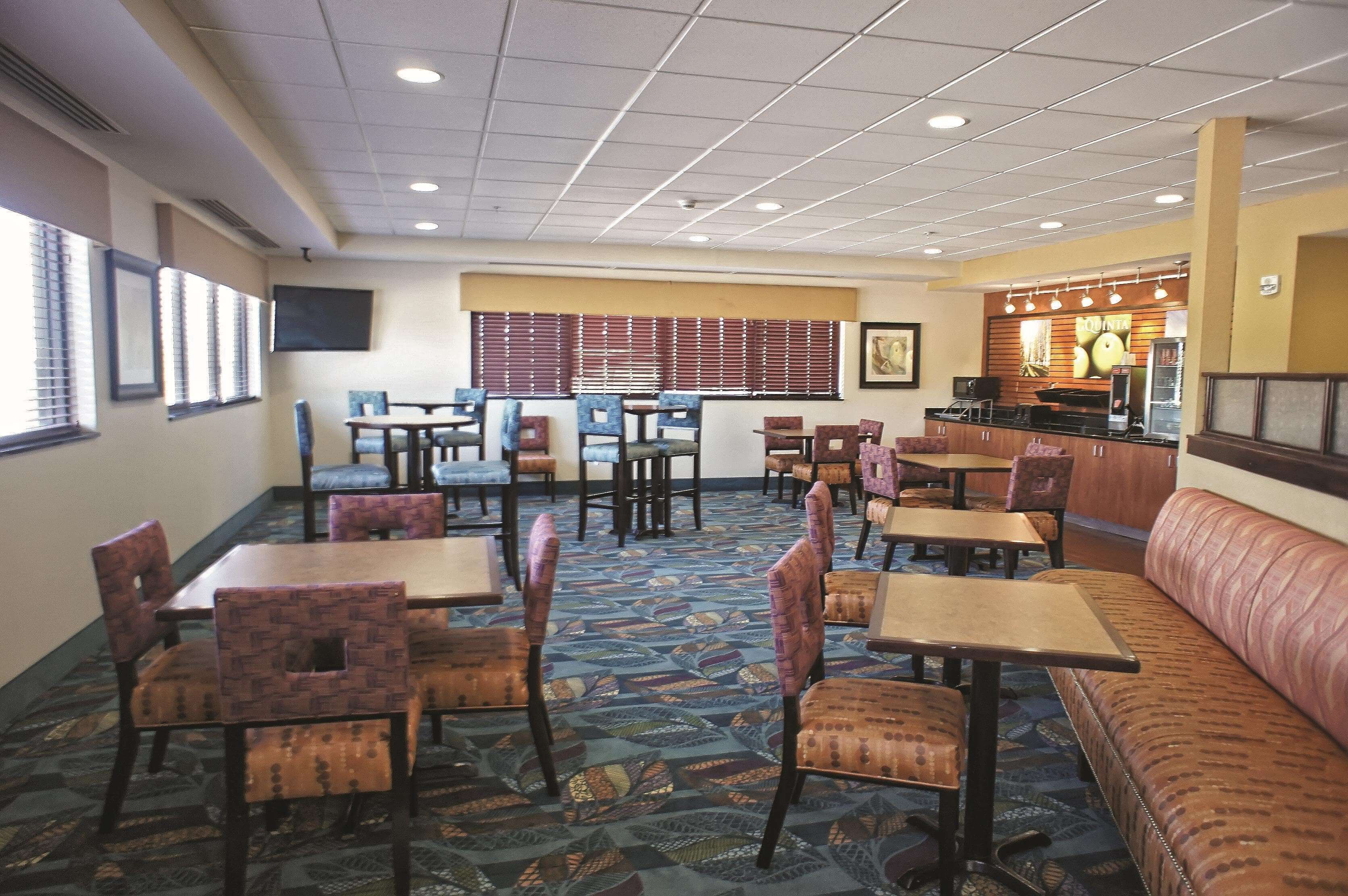 A hotel dining area with multiple tables and chairs, a sofa, and a counter with a menu display.