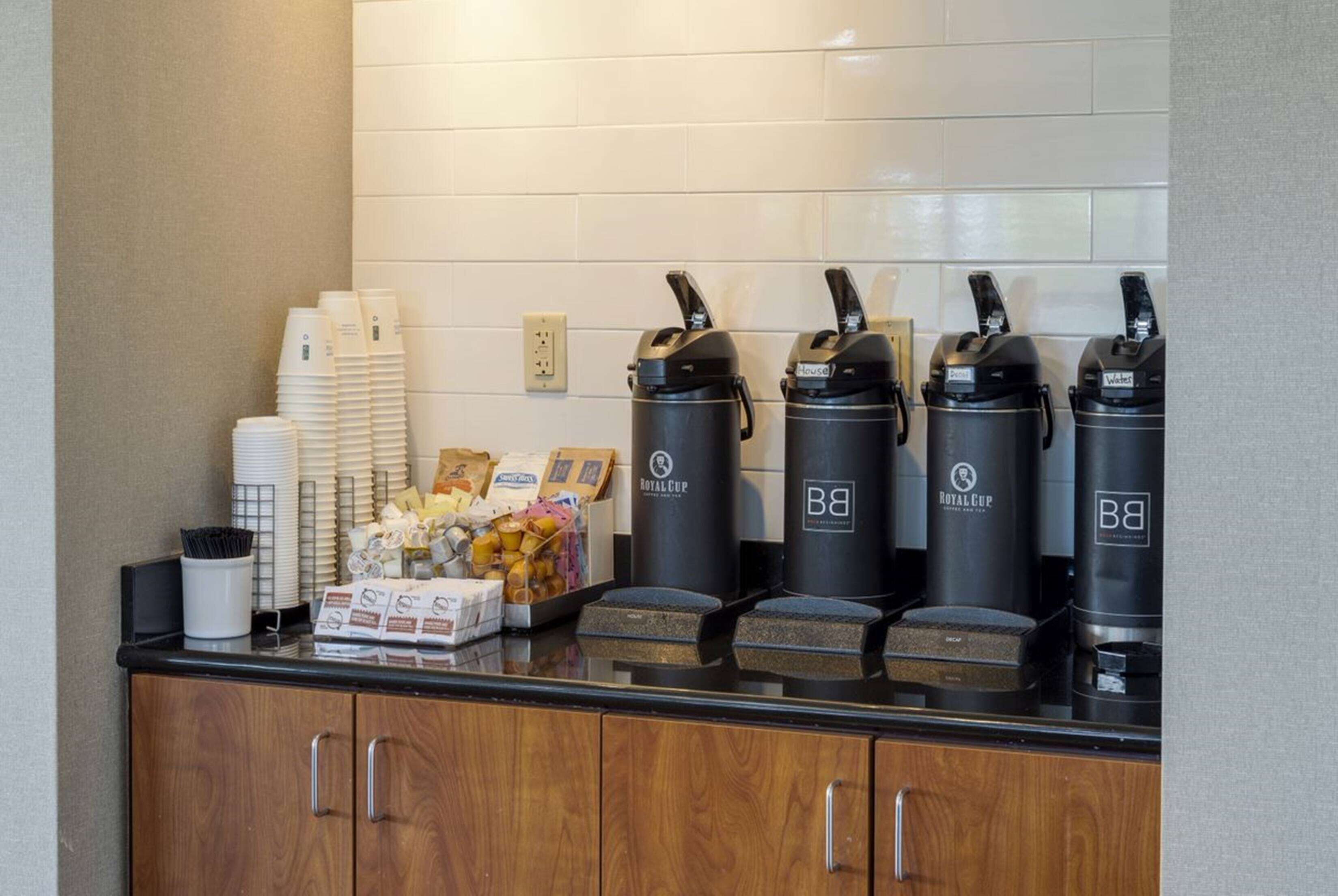 Un espace dédié au café, équipé de plusieurs distributeurs de café, de piles de gobelets jetables et d’une variété d’aliments.