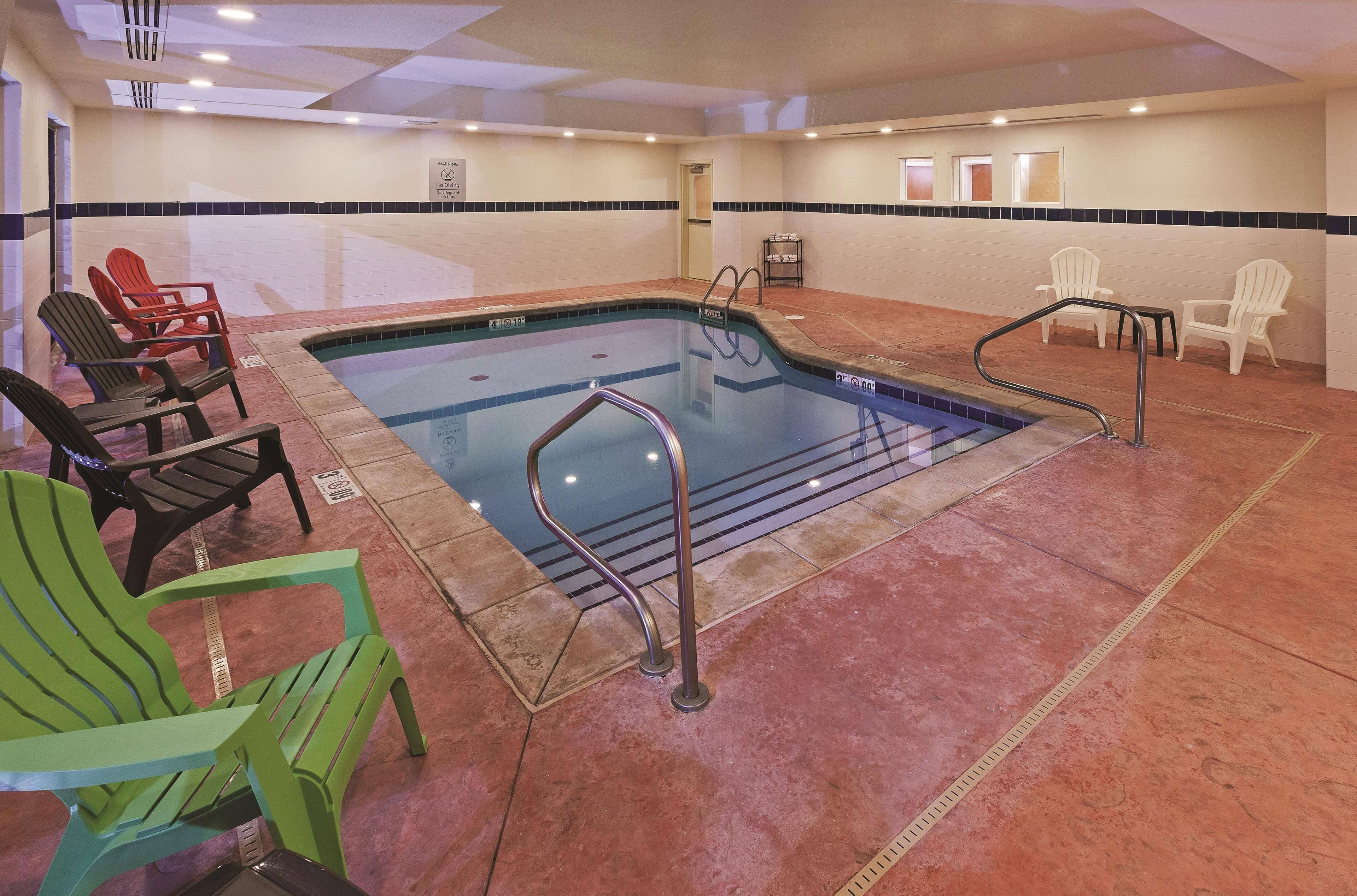 An indoor pool area with a pool, lounge chairs, and a changing room.