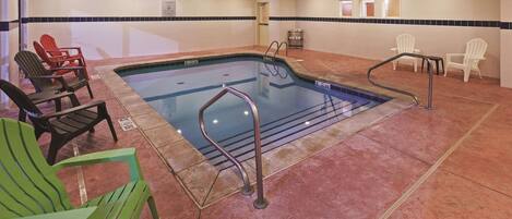 An indoor pool area with a pool, lounge chairs, and a changing room.