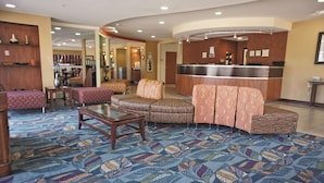 Un hall d'hôtel comprenant un comptoir d'accueil, un tapis à motifs et des espaces aménagés avec des sièges.
