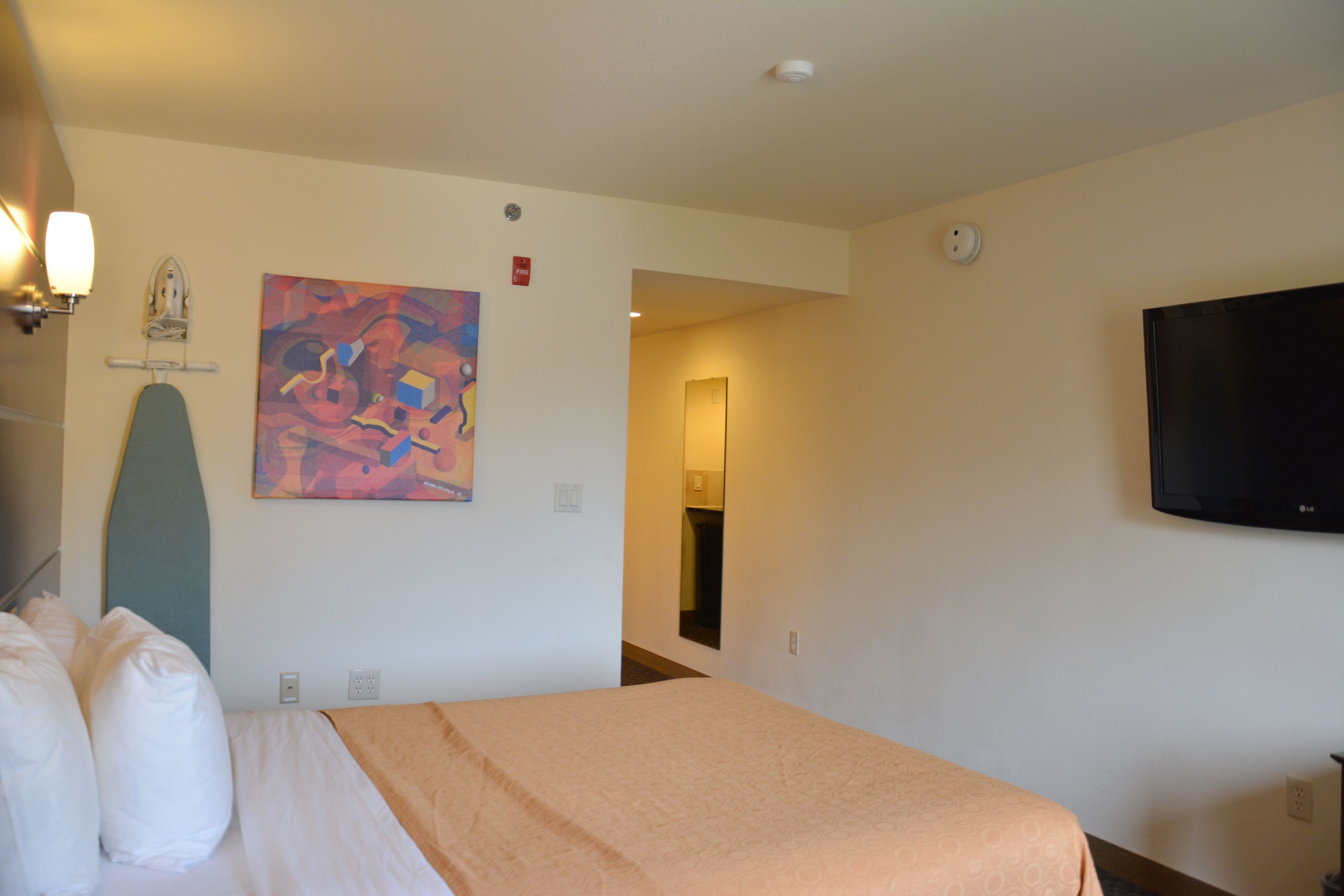 Une chambre d’hôtel avec un lit, un tableau, une télévision et une porte donnant sur une autre pièce.