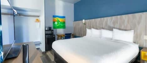 A hotel room with a large bed, a desk with a laptop, a TV, and a painting on the wall.
