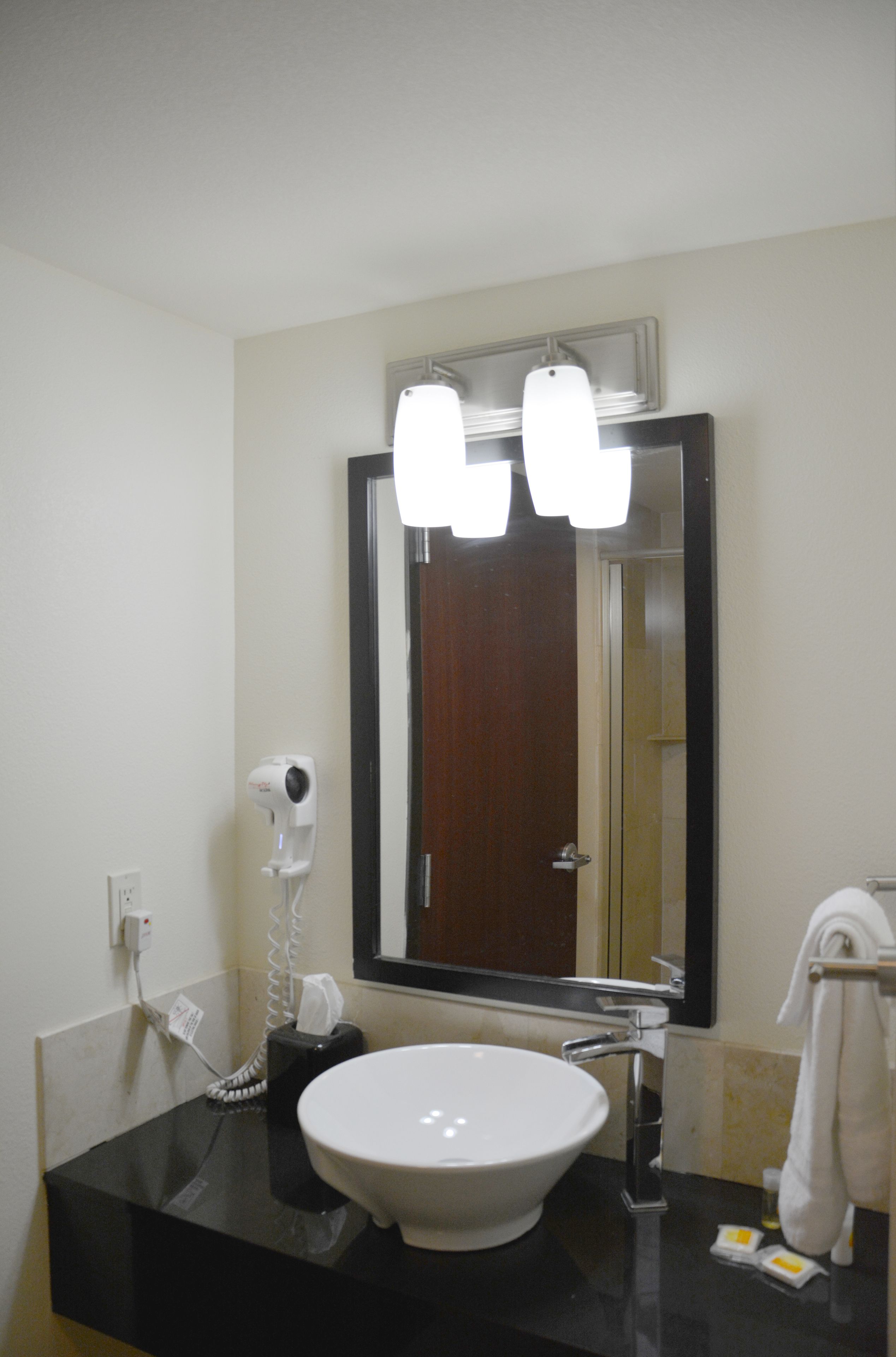 A bathroom with a black countertop, a white sink, a mirror, and a hair dryer.
