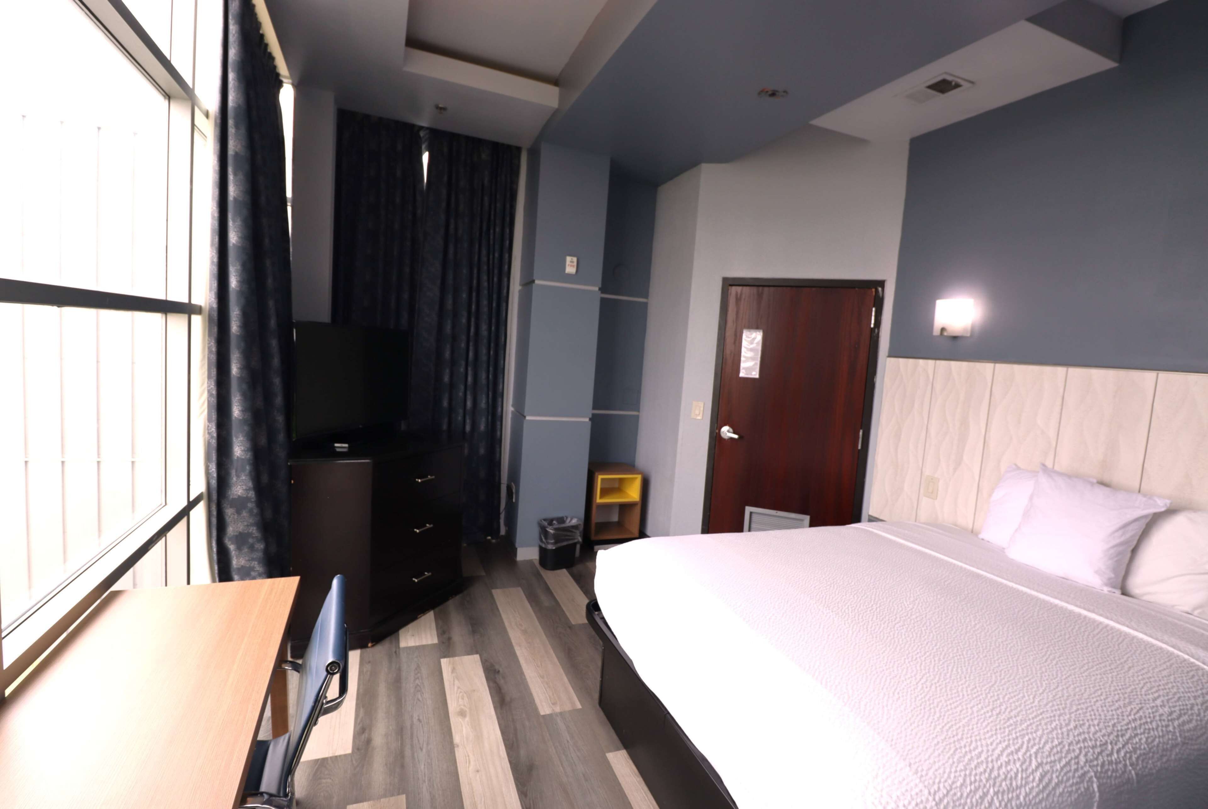 Een hotelkamer met een bed, een bureau, een stoel, een kledingkast, een televisie en een deur.