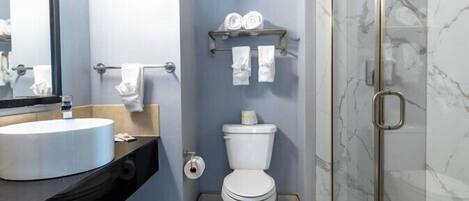 A modern bathroom with a round sink, toilet, and glass shower enclosure.