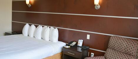 A hotel room with a large bed, a nightstand with a phone and a lamp, and a patterned armchair.