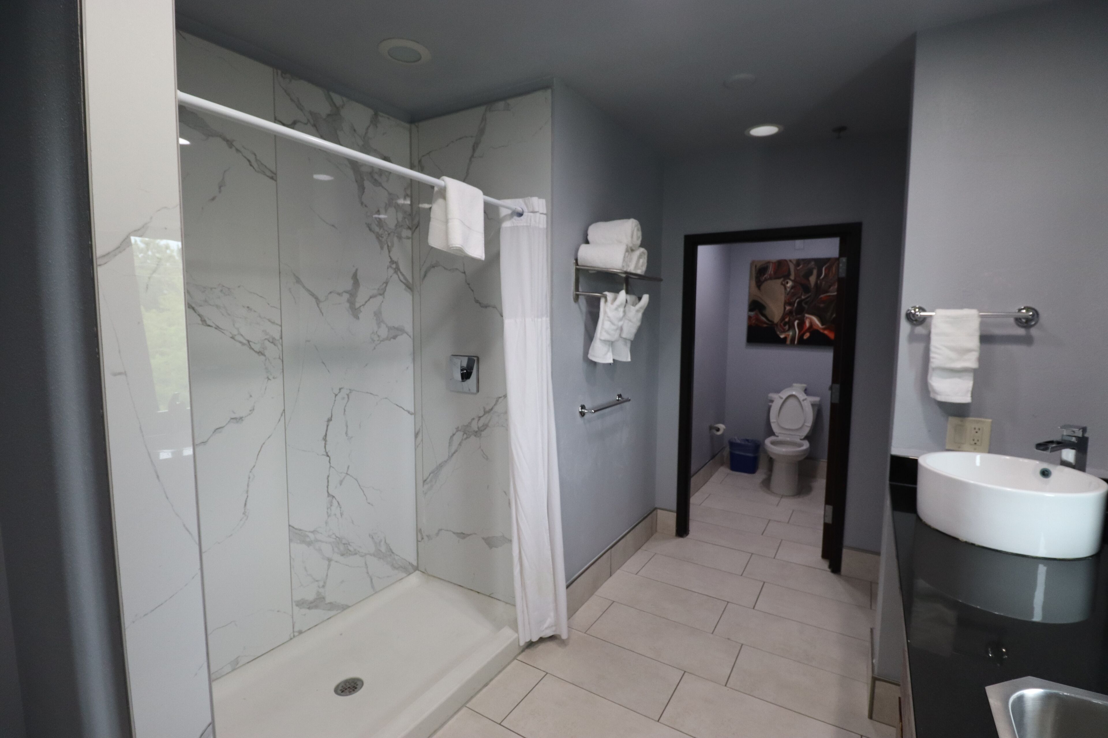 A modern bathroom with a marble shower, a sink, and a toilet.