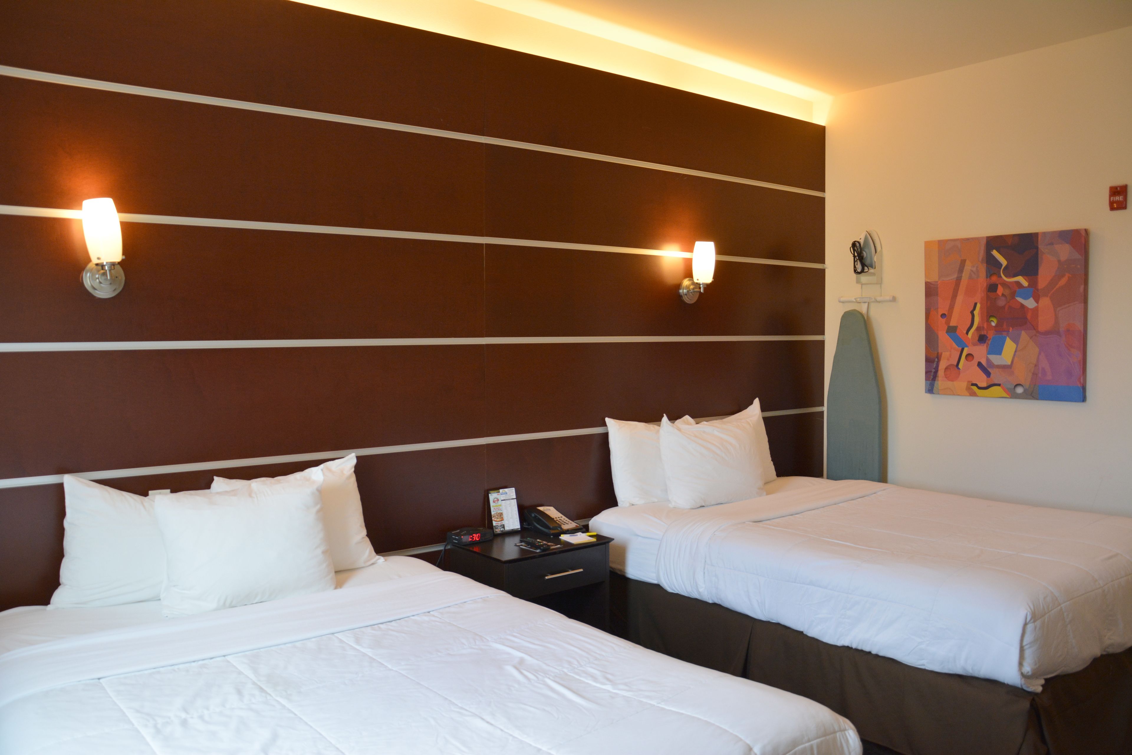 A hotel room with two beds, a nightstand with a phone and a clock, and a painting on the wall.