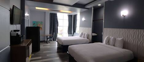 A modern hotel room with two beds, a desk, a TV, and a painting on the wall.