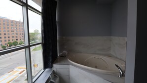 Un baño moderno con una bañera grande, una ventana con vistas a un paisaje urbano y un perchero para toallas.