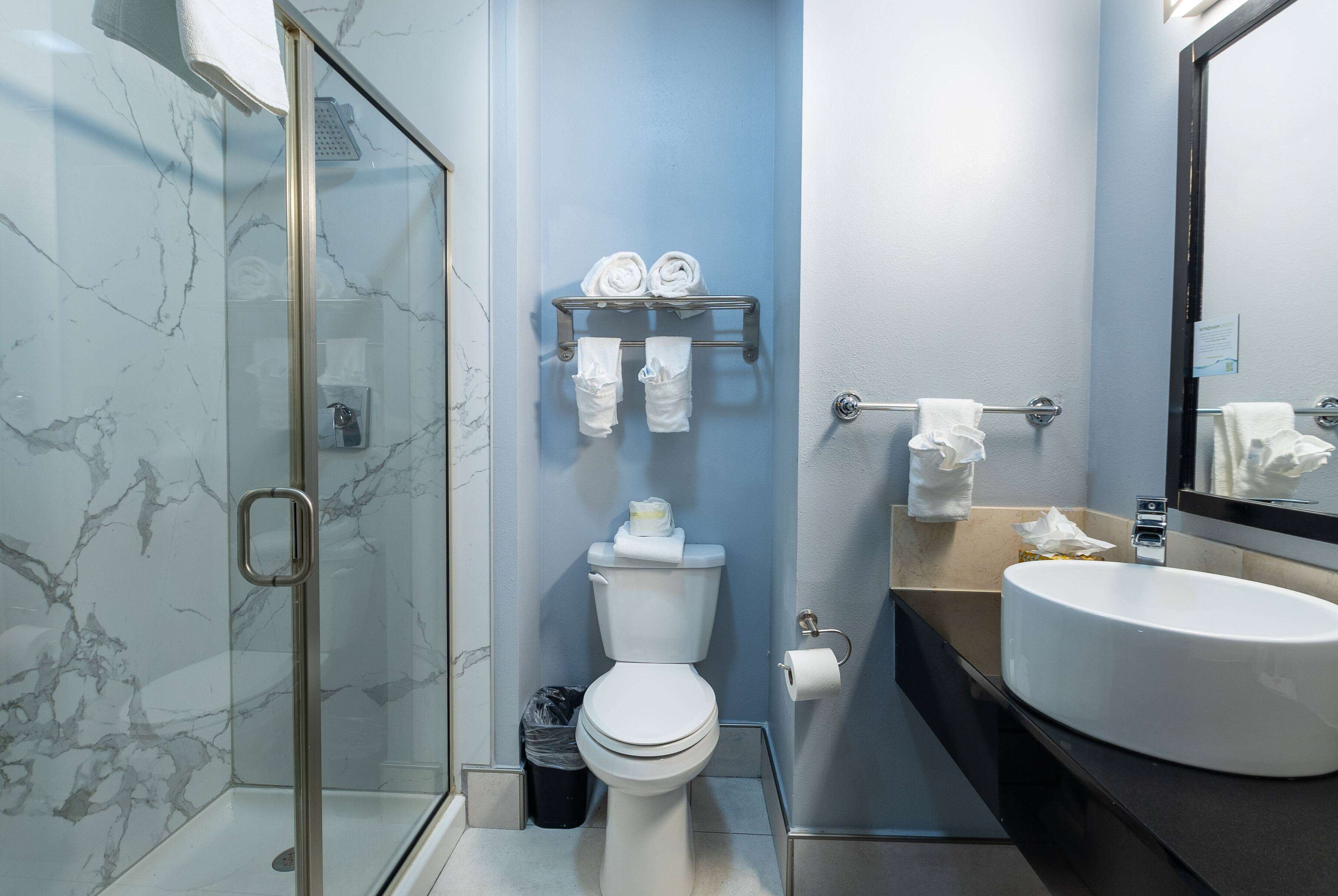 A bathroom with a glass shower enclosure, a white toilet, a towel rack with towels, a sink, and a mirror.