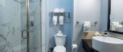 A bathroom with a glass shower enclosure, a white toilet, a towel rack with towels, a sink, and a mirror.