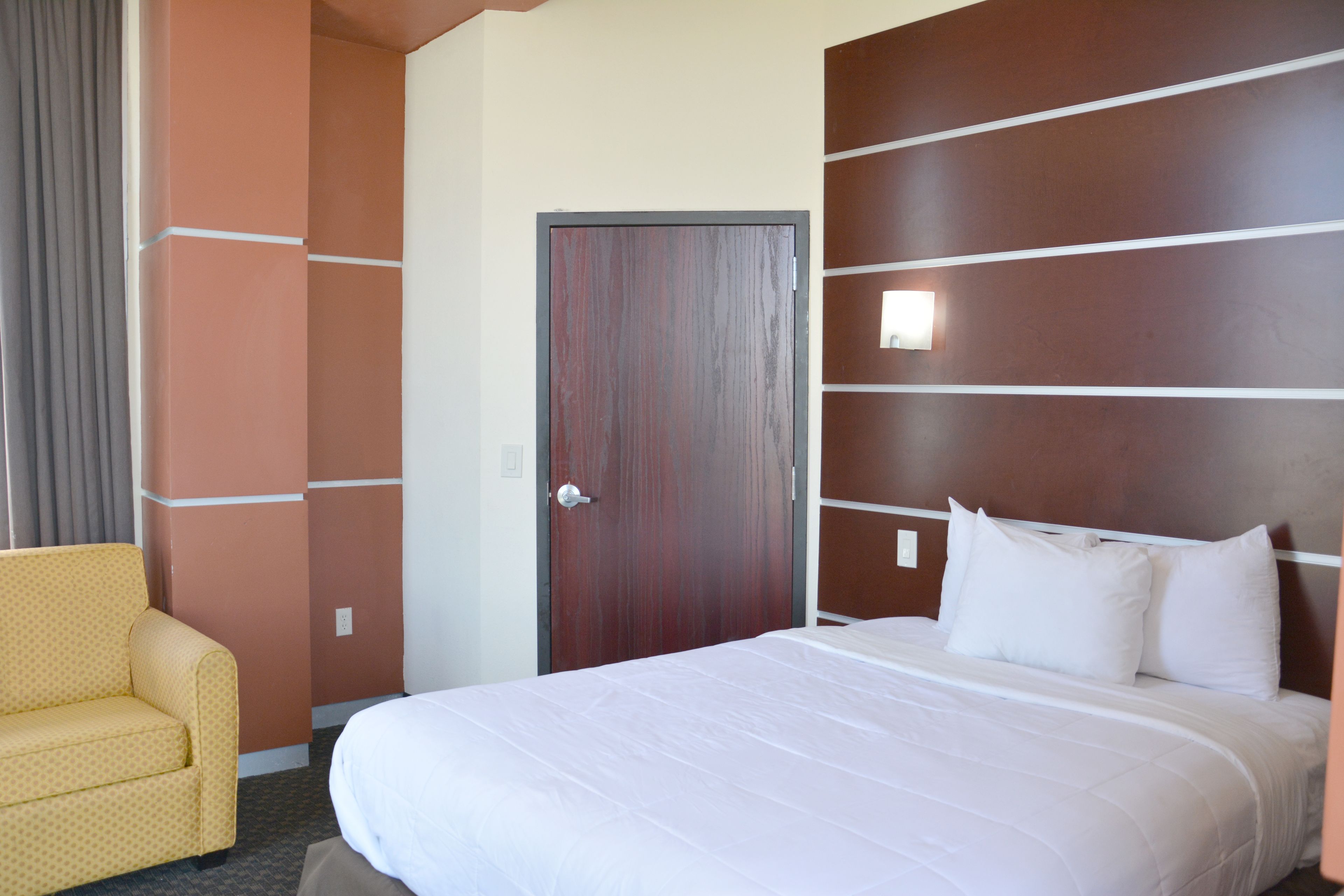 Een hotelkamer met een groot bed, een gele fauteuil en een wand van houten panelen.