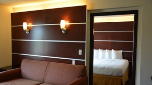 Habitación de hotel con un sofá marrón, una cama con ropa de cama blanca y dos luces fijadas a la pared.