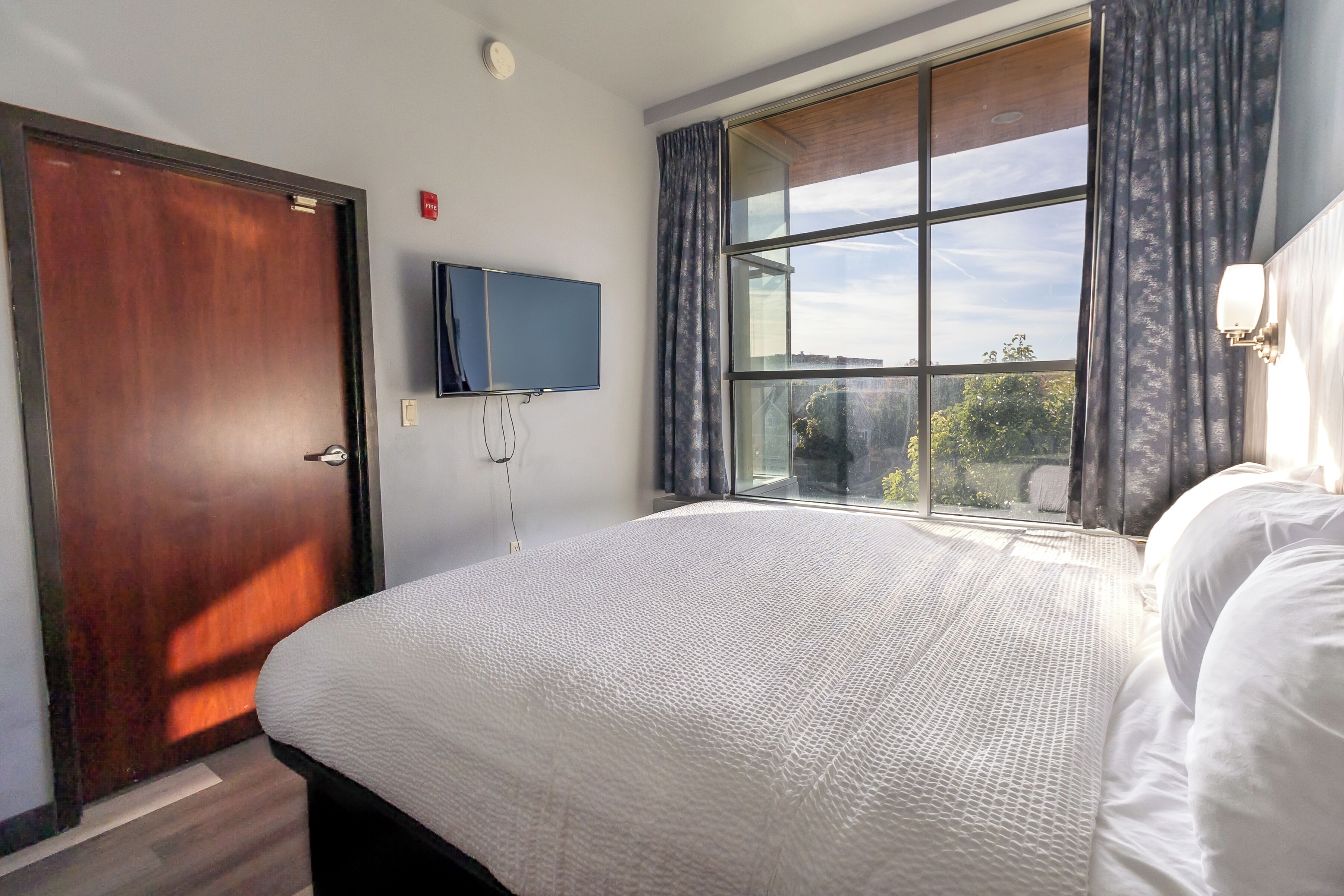 A hotel room with a large bed, a television mounted on the wall, and a window with curtains.