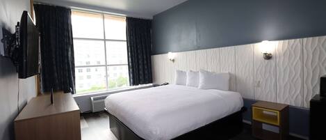 A modern hotel room with a large bed, a flat-screen TV, a desk, and a window with curtains.