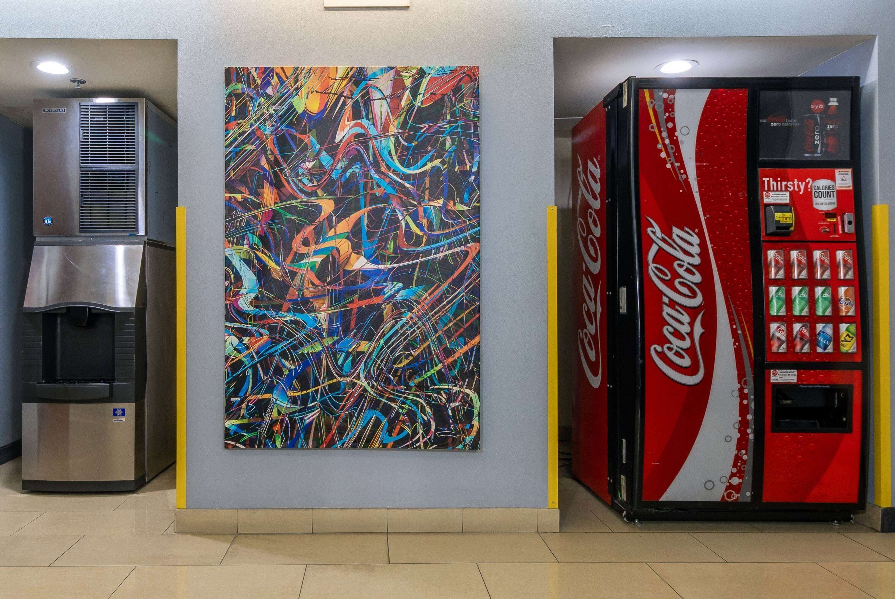 Un distributeur automatique, un point d’eau et une peinture abstraite aux couleurs vives sur un mur.