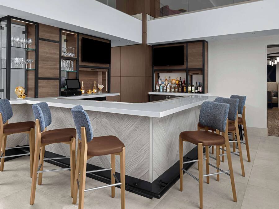 A modern bar area with a marble countertop, wooden bar stools, and a wine rack.
