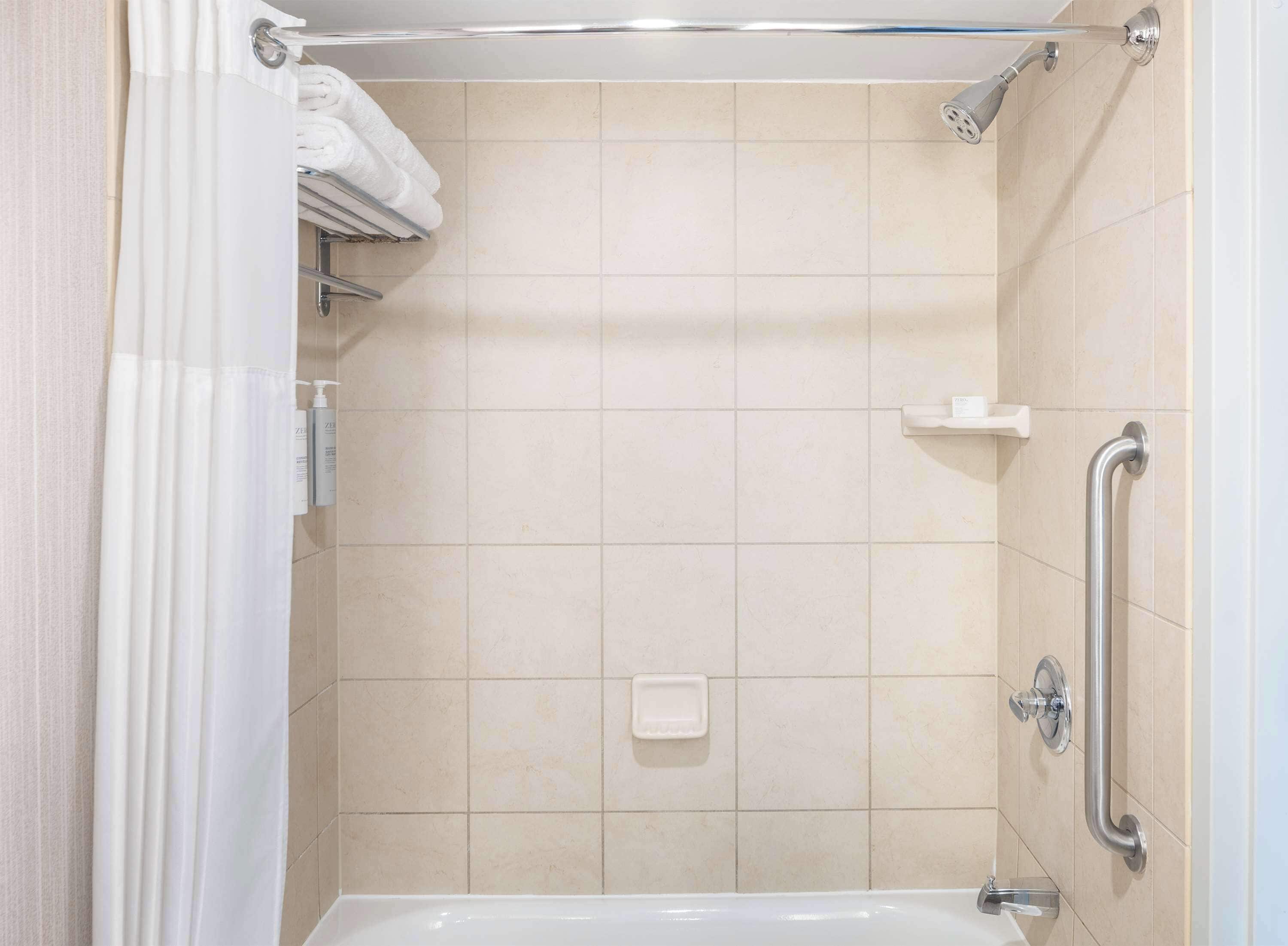 Un angolo doccia con maniglia di sostegno, ripiano con articoli da toilette e porta asciugamani.