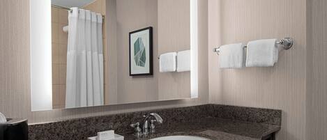 A modern bathroom with a granite countertop sink, a framed artwork on the wall, and a towel rack with two towels.