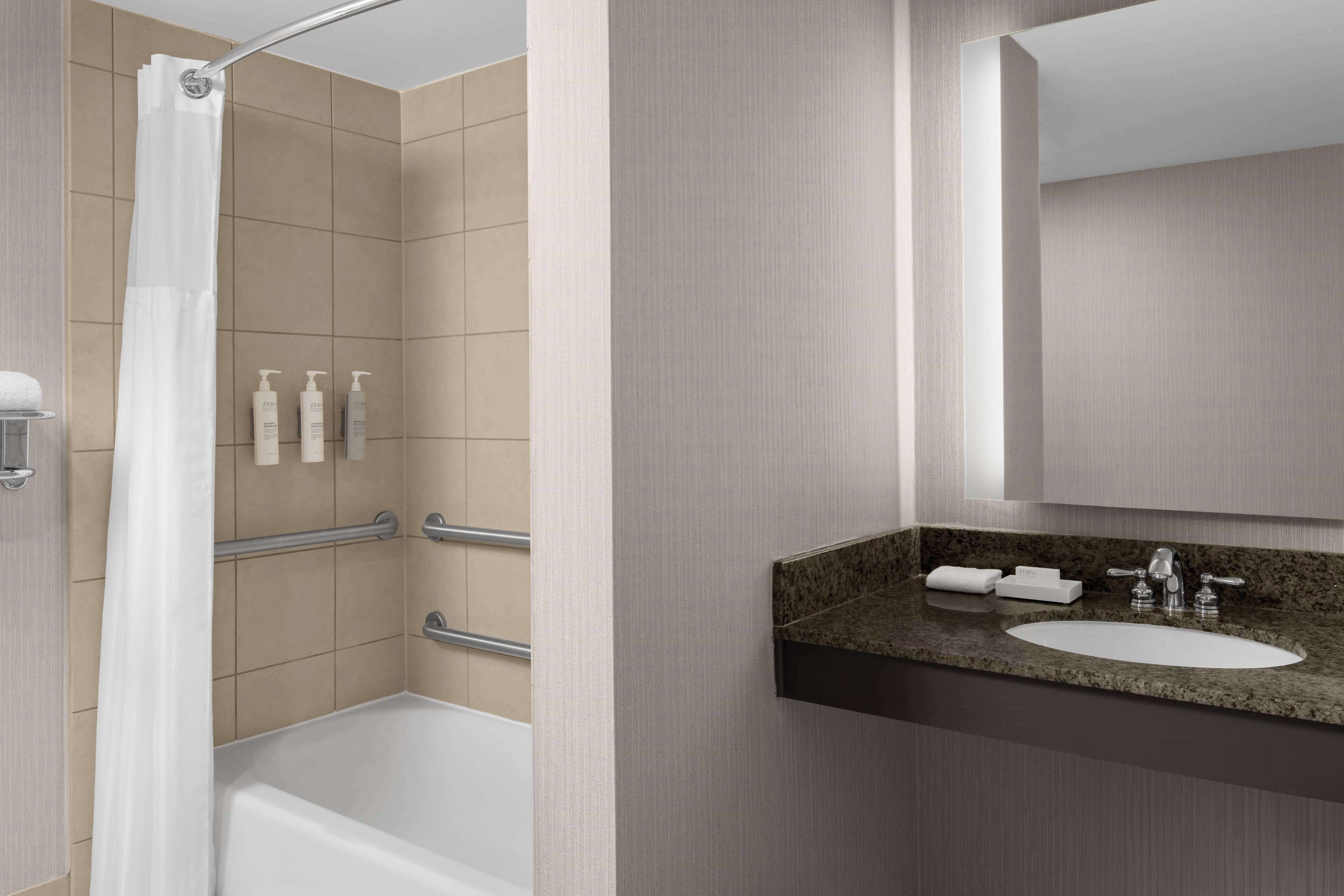 Ein modernes Badezimmer mit Badewanne, Dusche mit weißer Duschvorhang, Waschtisch mit Granitplatte und Spiegel über dem Waschbecken.