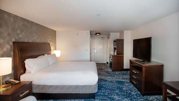 A hotel room with a large bed, a desk with a lamp, a television, and a wardrobe.