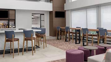 A modern bar area with seating, a counter with bottles, and a TV mounted on the wall.