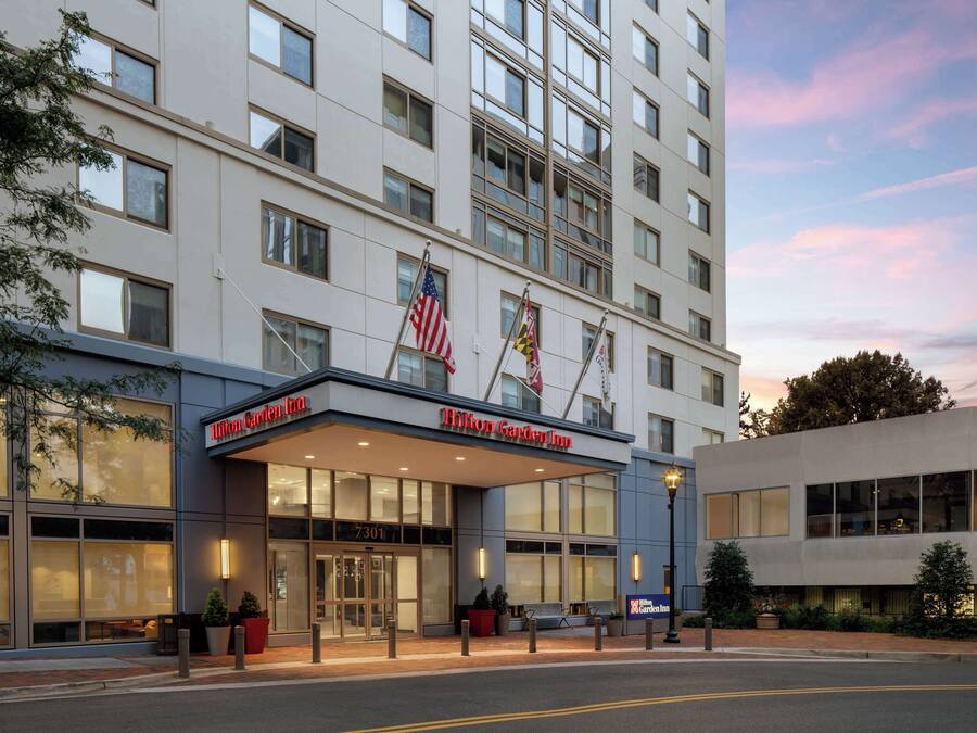 Un Hilton Garden Inn con fachada moderna, amplias ventanas y una bandera estadounidense.
